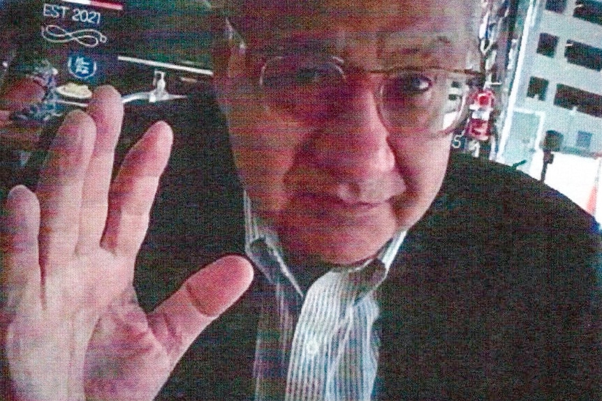 Elderly man waves at camera wearing glasses 