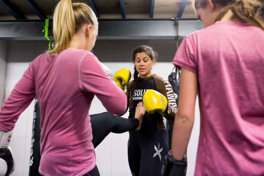 Shantelle Thompson wears boxing gloves while training two women.
