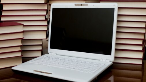 A laptop sits in front of a pile of books (Thinkstock: iStockphoto)