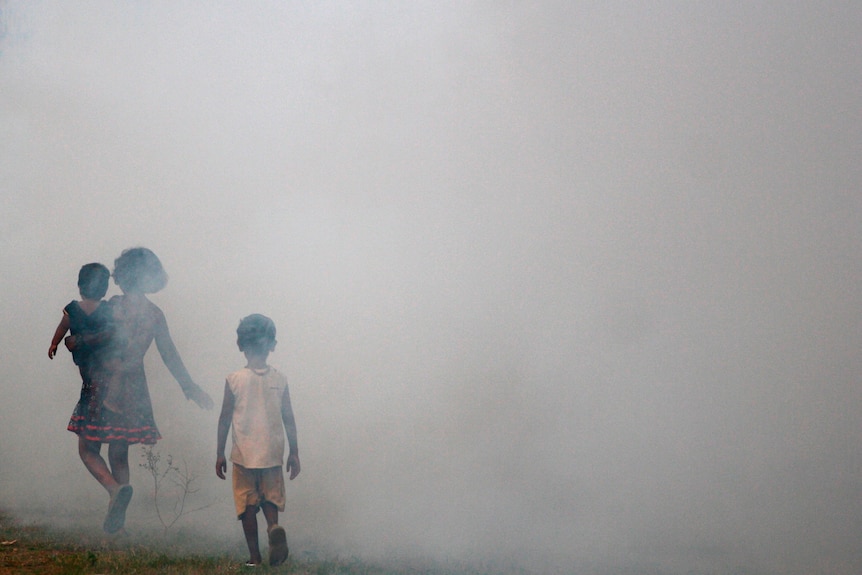 Children of local residents walk through an area being fumigated by municipal workers near to one of the venues for the Commonwealth Games on the outskirts of New Delhi