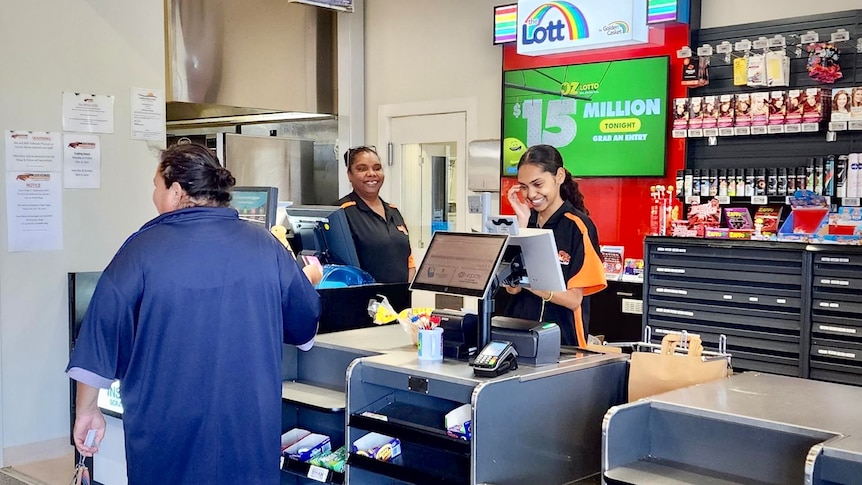 Two Indigenous cashiers laugh at a supermarket