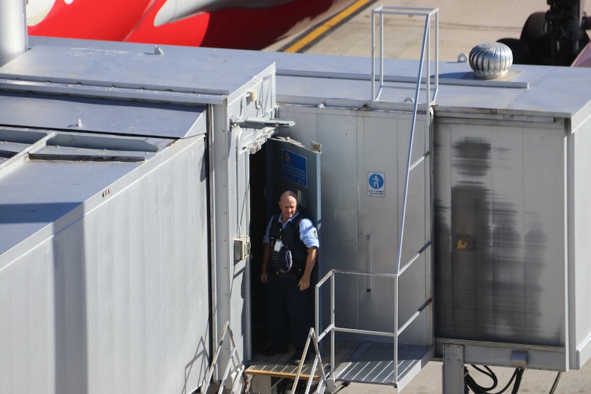 A police officer stands on a gangway next to a plane at Perth International Airport.