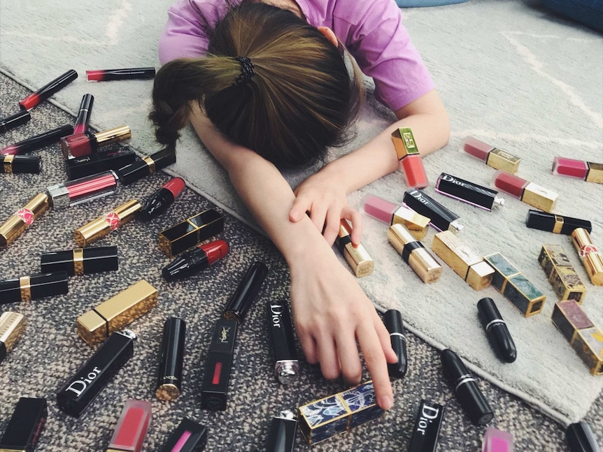Young Chinese woman fell over with many lipsticks scattering around in a living room.
