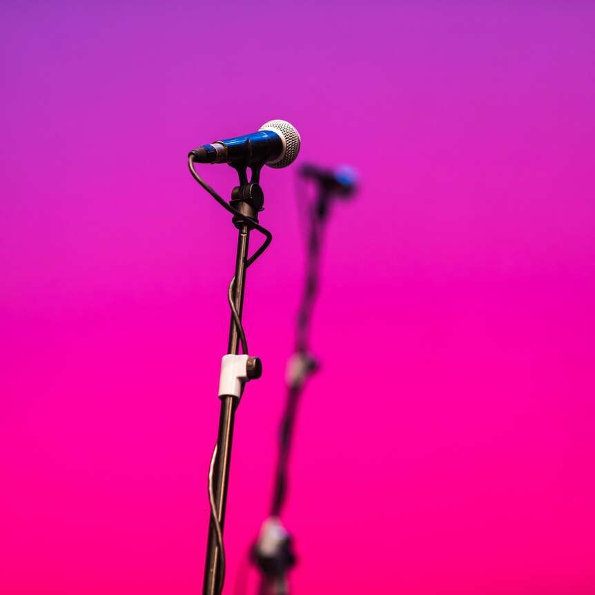 A microphone on a stand in front of a pink background. 