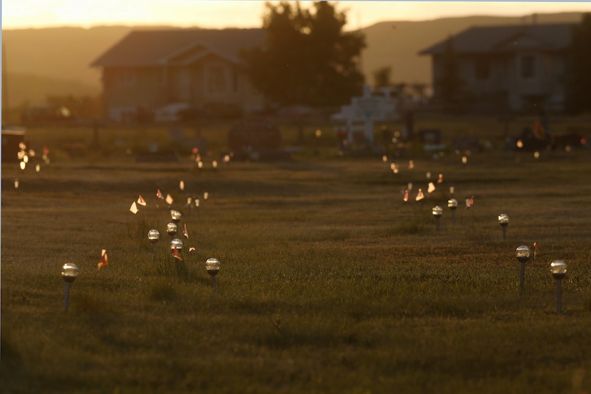 Solar lights line rows of unmarked graves in a field near a house