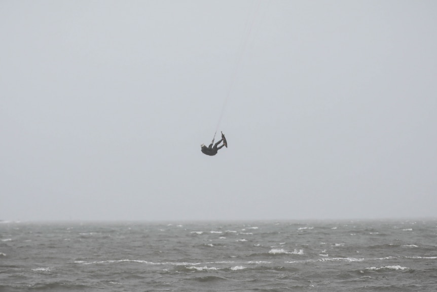 A kitesurfer gets airtime several metres above the ocean water amid choppy conditions and bad weather.