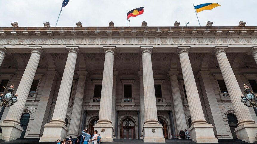 A group sits on the stairs in front of Victoria's parliament house.