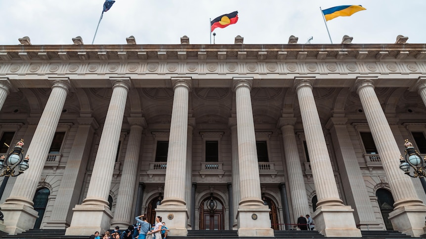 A group sits on the stairs in front of Victoria's parliament house.