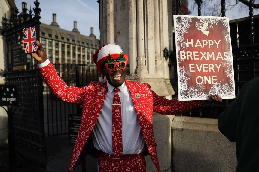 A man in a santa hat holding a sign reading "Happy Brexmas Every One"