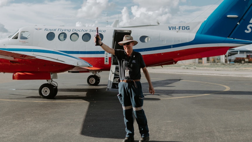 man holds up bottle of champagne with plane in background