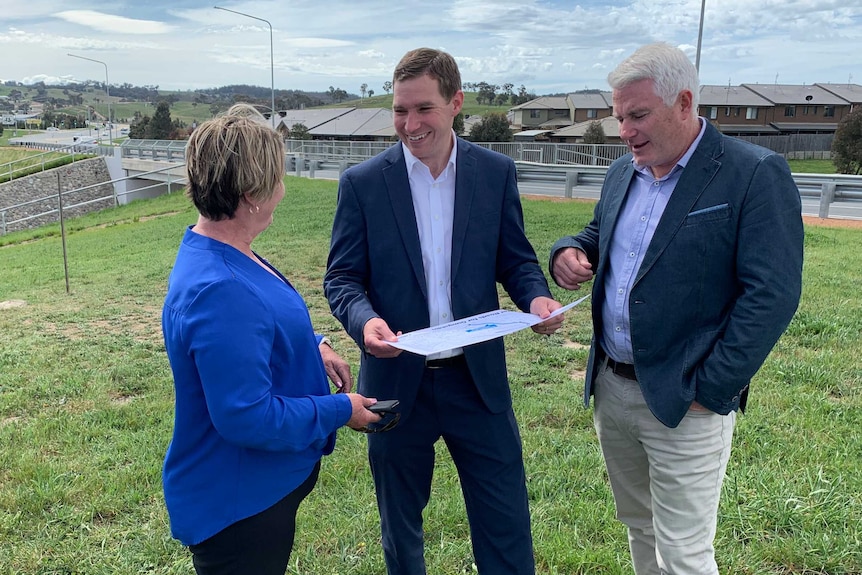 A woman and two men stand in a suburb grassed area.