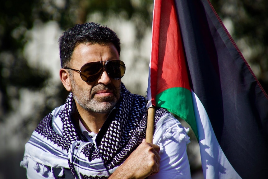 A photo of Nasser wearing sunglasses and a Palestinian national identity scarf 'Kufeyeh' holding a Palestinian flag 