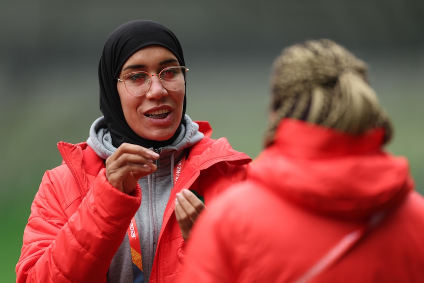 A woman wearing a headscarf talks tactics with a coach on the sideline in Melbourne ahead of World Cup match. 