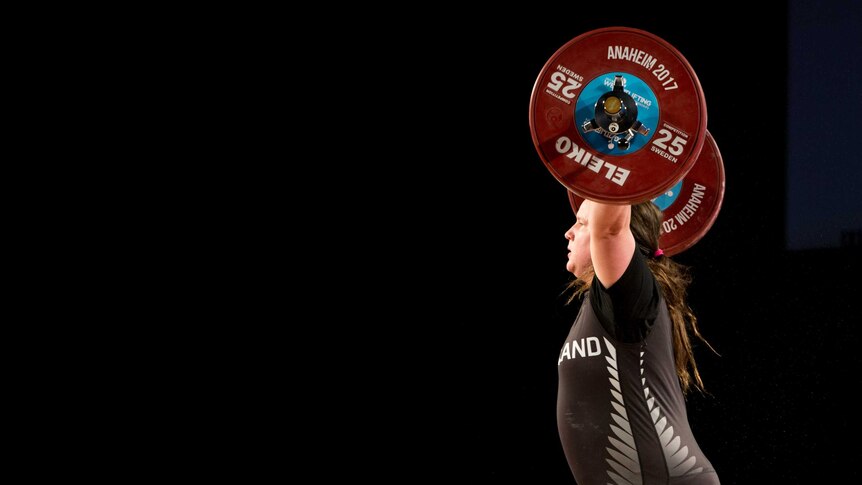 Laurel Hubbard holds the bar and weights above her head during a weightlifting competition.
