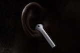 Apple vice president Phil Schiller on stage in front of a screen with wireless headphones