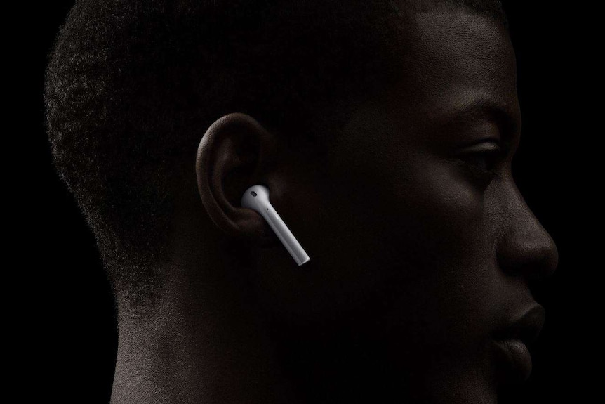 Apple vice president Phil Schiller on stage in front of a screen with wireless headphones