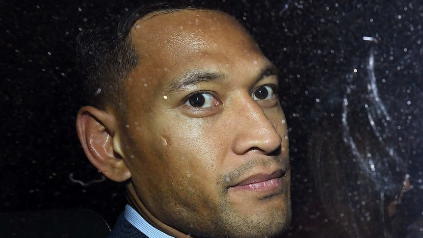 Israel Folau, wearing a suit, looks out a car window.