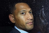 Israel Folau, wearing a suit, looks out a car window.