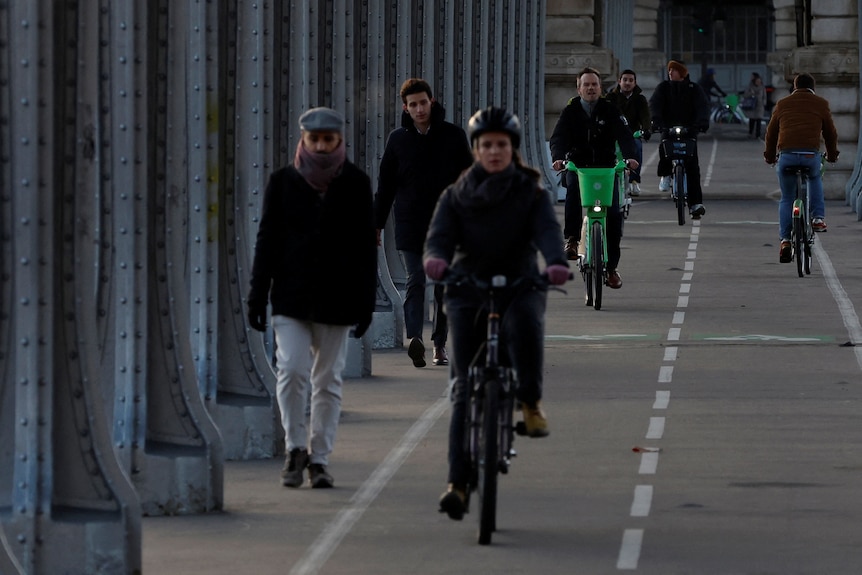 French people in dark winter clothing walk and ride bicycles along a bridge path.