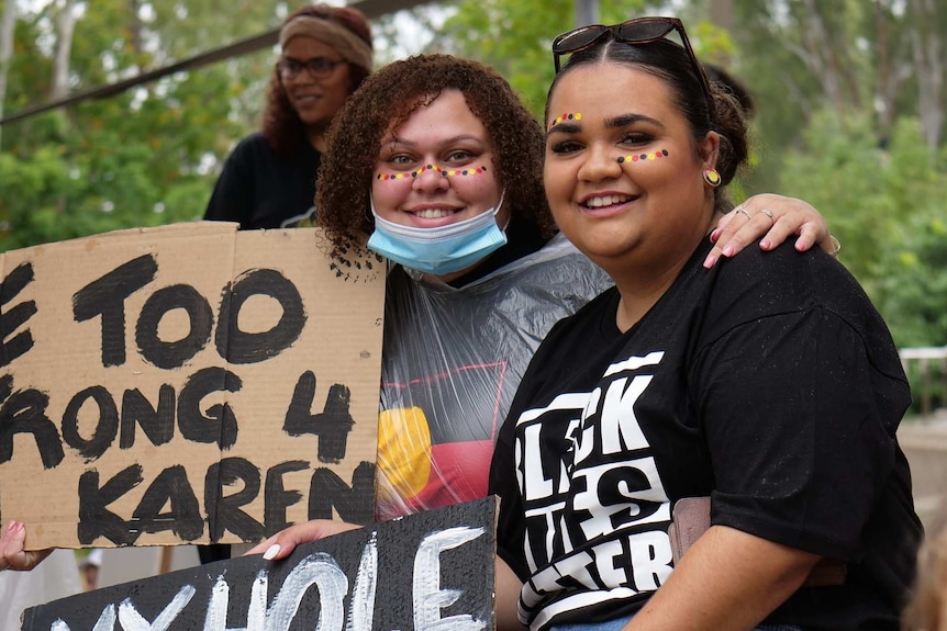 Letitia Smith and her friend smile holding up placards with their faces painted with yellow, black and red dots.