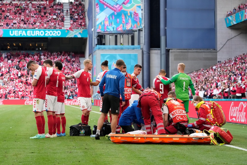 Medical professionals attend to Christian Eriksen as his teammates form a barrier in front of him