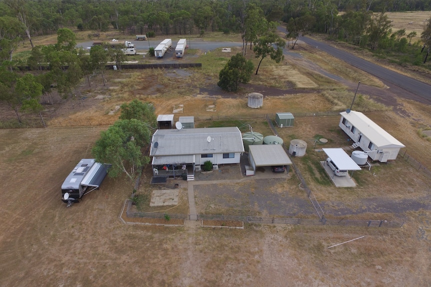 An overhead photo of a school in remote area, shurbs, trees around a brown paddock, with a few buildings.