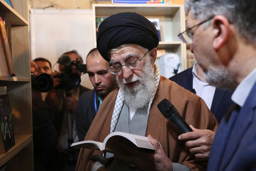 Supreme Leader Ayatollah Ali Khamenei reads part of a book into a microphone while visiting Tehran's book fair.