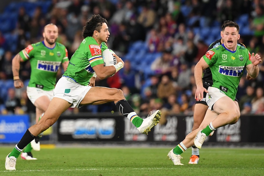 A Canberra Raiders NRL player strides out as he runs with the ball against Cronulla.