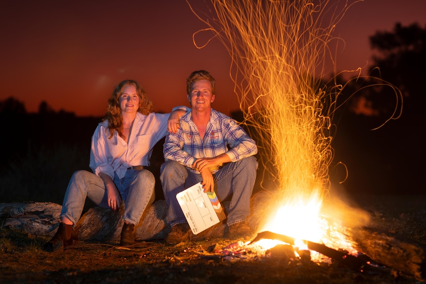 Woman and man sit by campfire
