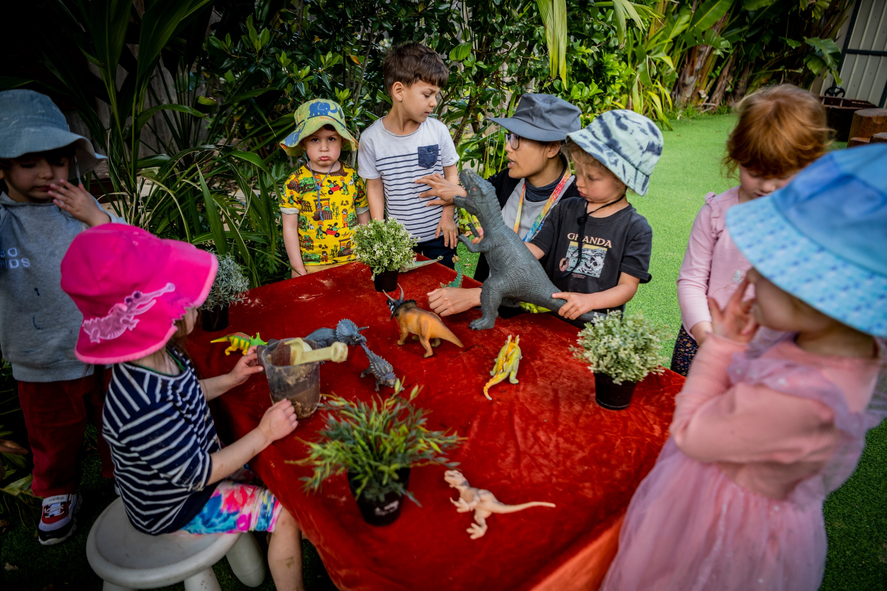 A group of young kids at a childcare centre standing around a table with toy dinosaurs 