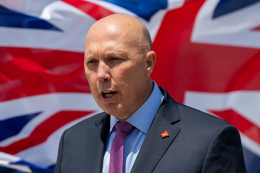 Man in a suit speaks with Australian flag in the background