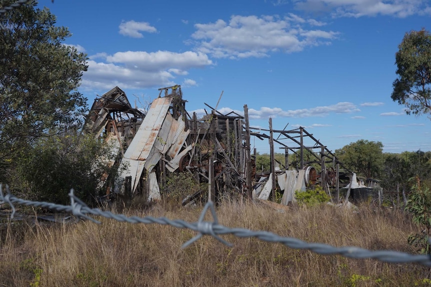 Barbed wire separates humans and the demolished state battery which is largely a bunch of wooden structures and corrugated iron.