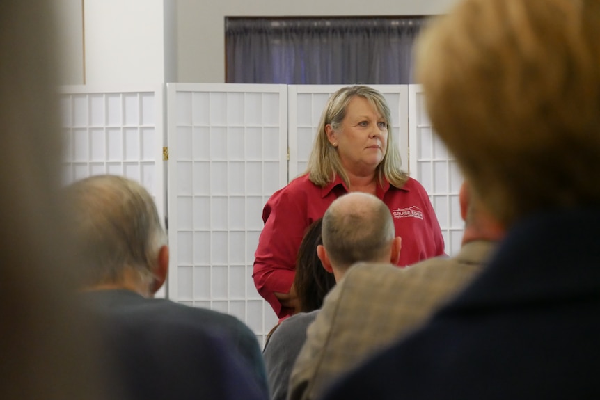 a woman addressing a crowd of people. she is wearing a red shirt