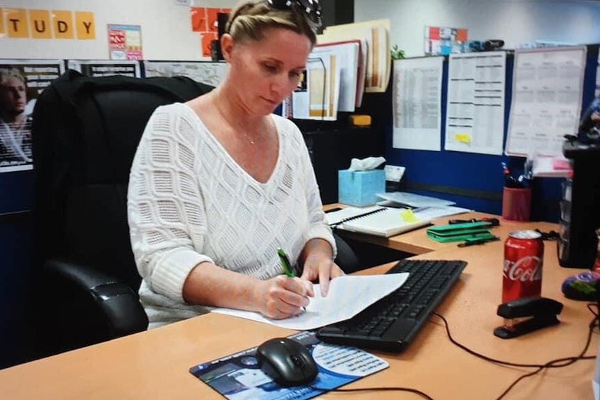 A lady sits at a desk writing.