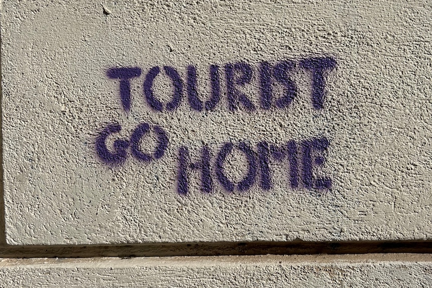 A stencilled graffiti on a stone wall saying "Tourist go Home".