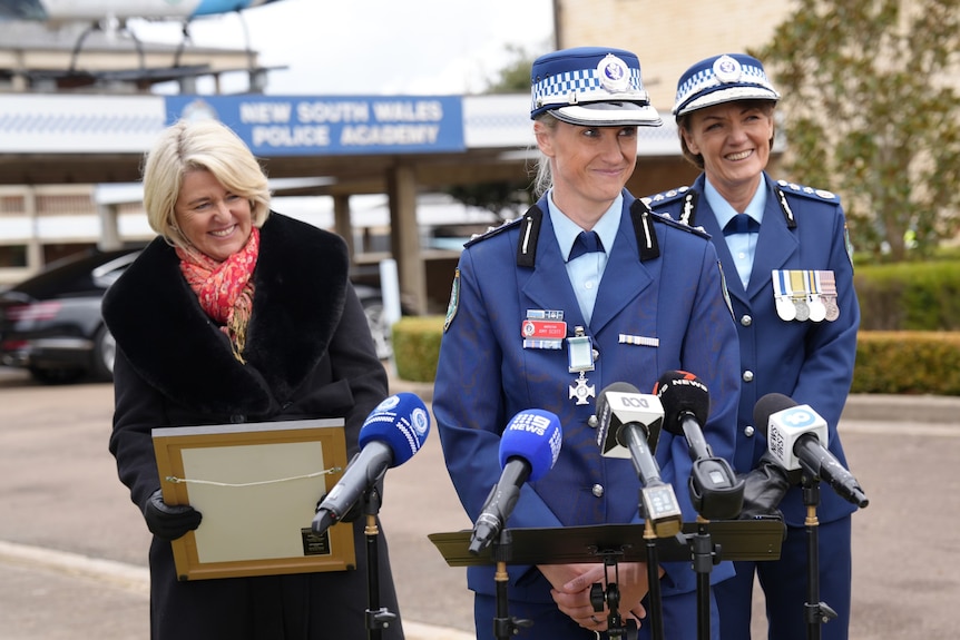 Amy Scott wearing a police uniform in front of microphones, in front of Premier, Police Commissioner and Police Minister