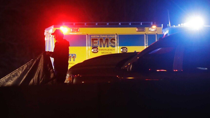 An emergency medical services vehicle is parked with its lights on while and emergency services officer works around it.