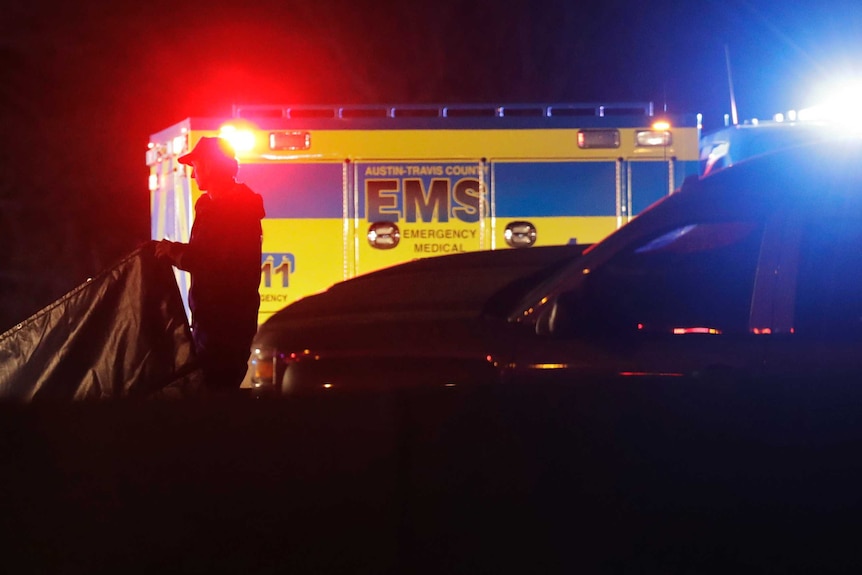 An emergency medical services vehicle is parked with its lights on while and emergency services officer works around it.