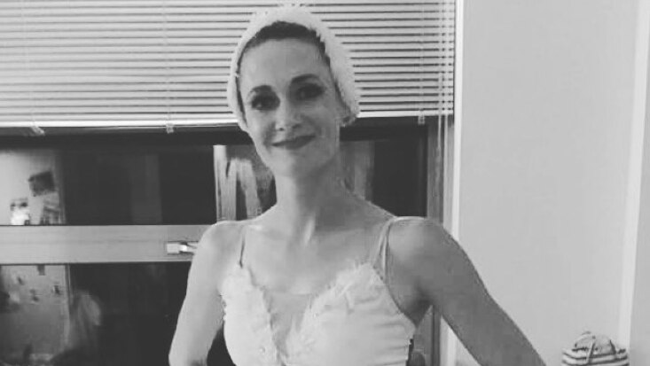 A ballerina in costume smiles as she poses for a photo with her hands on her hips