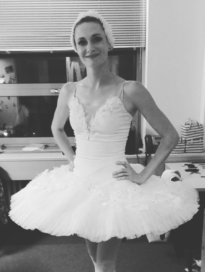 A ballerina in costume smiles as she poses for a photo with her hands on her hips