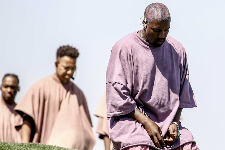 Kanye West in purple shirt kneeling and praying, during Sunday Service Coachella performance in 2019.