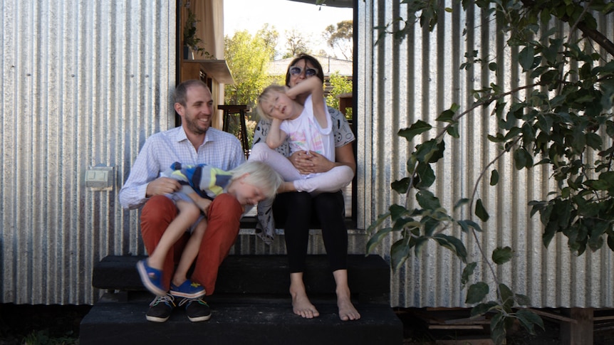 Builder and designer Quentin Irvine and his family sitting on the front step of their house.