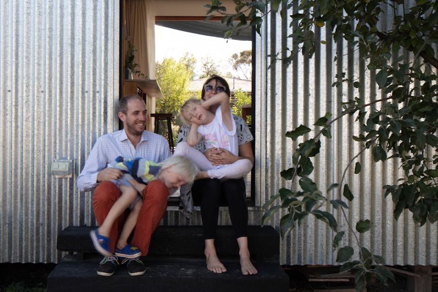 Builder and designer Quentin Irvine and his family sitting on the front step of their house.