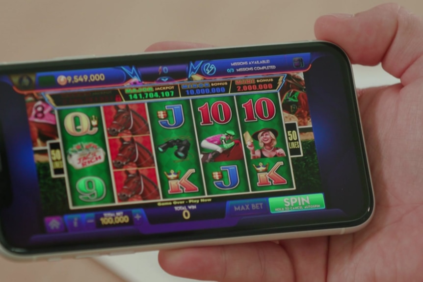 A person holds up a smartphone showing a poker machine style game in play