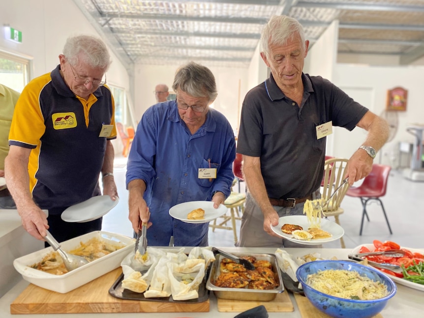 three men serving food onto their plate in a commercial kitchen