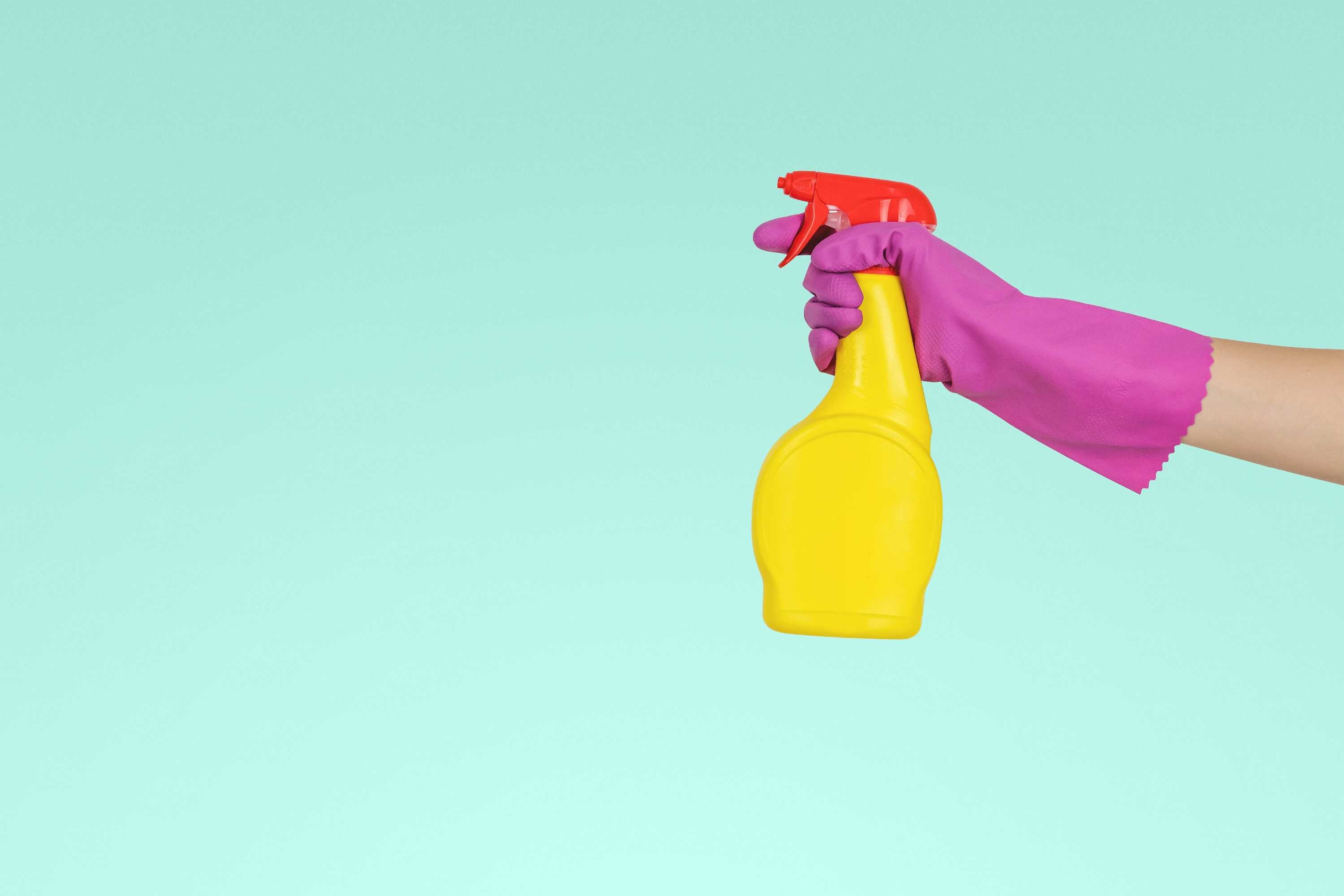Hand with rubber glove holding spray bottle with blank background for a story about cleaning your home without harsh chemicals.