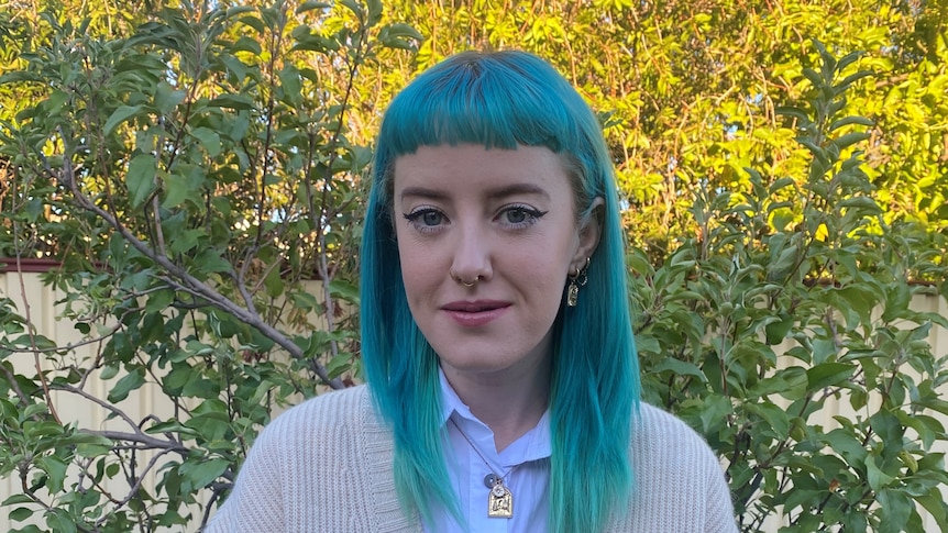 Madi - a young woman with blue-green hair, standing in front of a tree