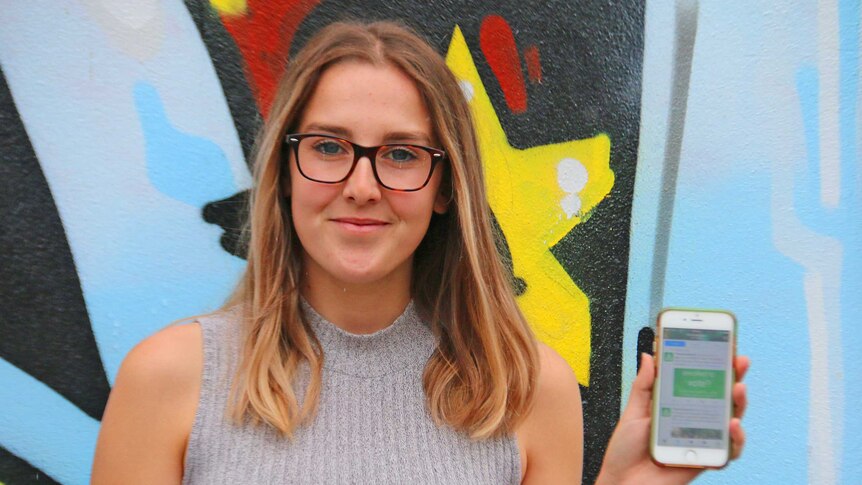 Girl in her mid 20s holding smartphone in front of mural