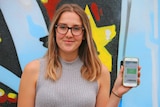 Girl in her mid 20s holding smartphone in front of mural