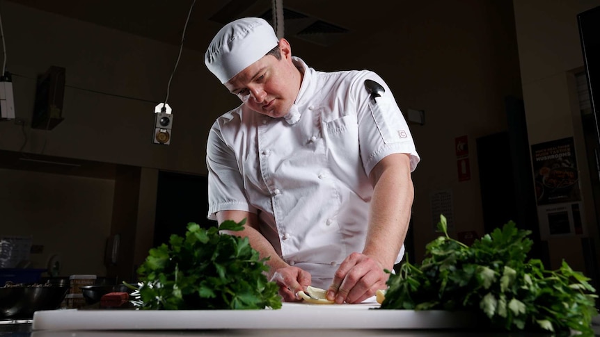 A man wearing a cook's outfit cutting up vegetables